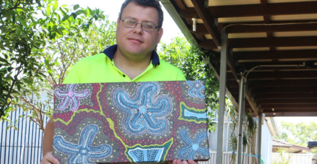 Joseph Formosa sitting in backyard holding one of his paintings.