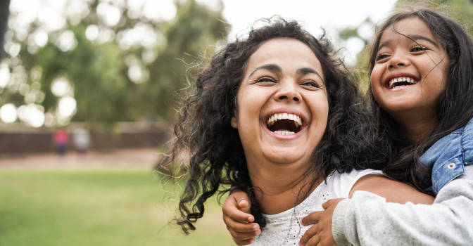 Mother carrying daughter on her back, laughing in a park