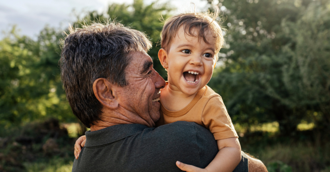 Grandfather holding child up, laughing outside.