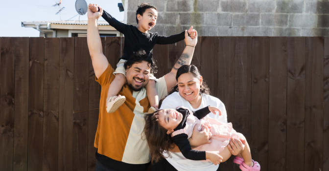 Family holding children, laughing in backyard.