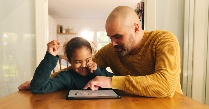 Father and daughter at table pointing at ipad