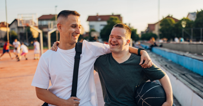 Man with disability and his friend walking away from a basketball court, holding a ball.