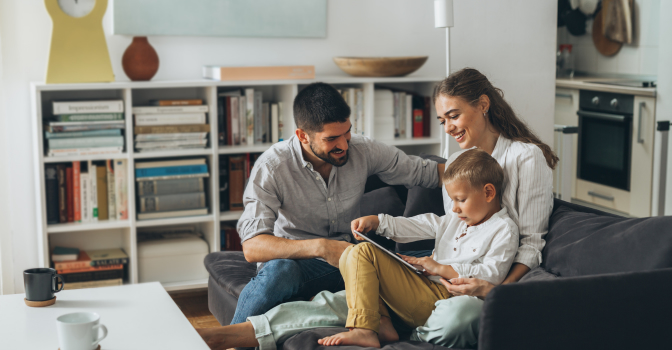 Young child, sitting on the couch with his parents, looking at an ipad.