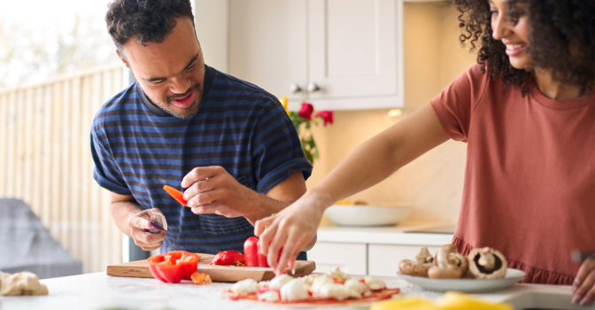 Young man with disability and his carer cooking in the kitchen.