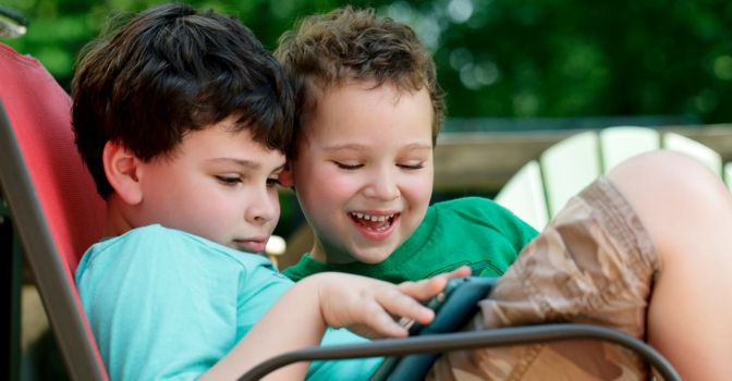 Two young boys sitting on a chair together watching something on a tablet