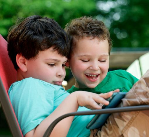Two young boys sitting on a chair together watching something on a tablet