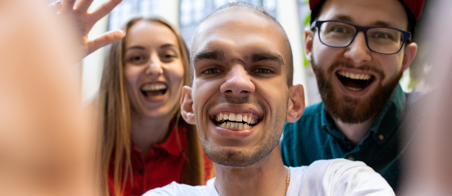 Young person with disability, taking a selfie with his friends behind him.